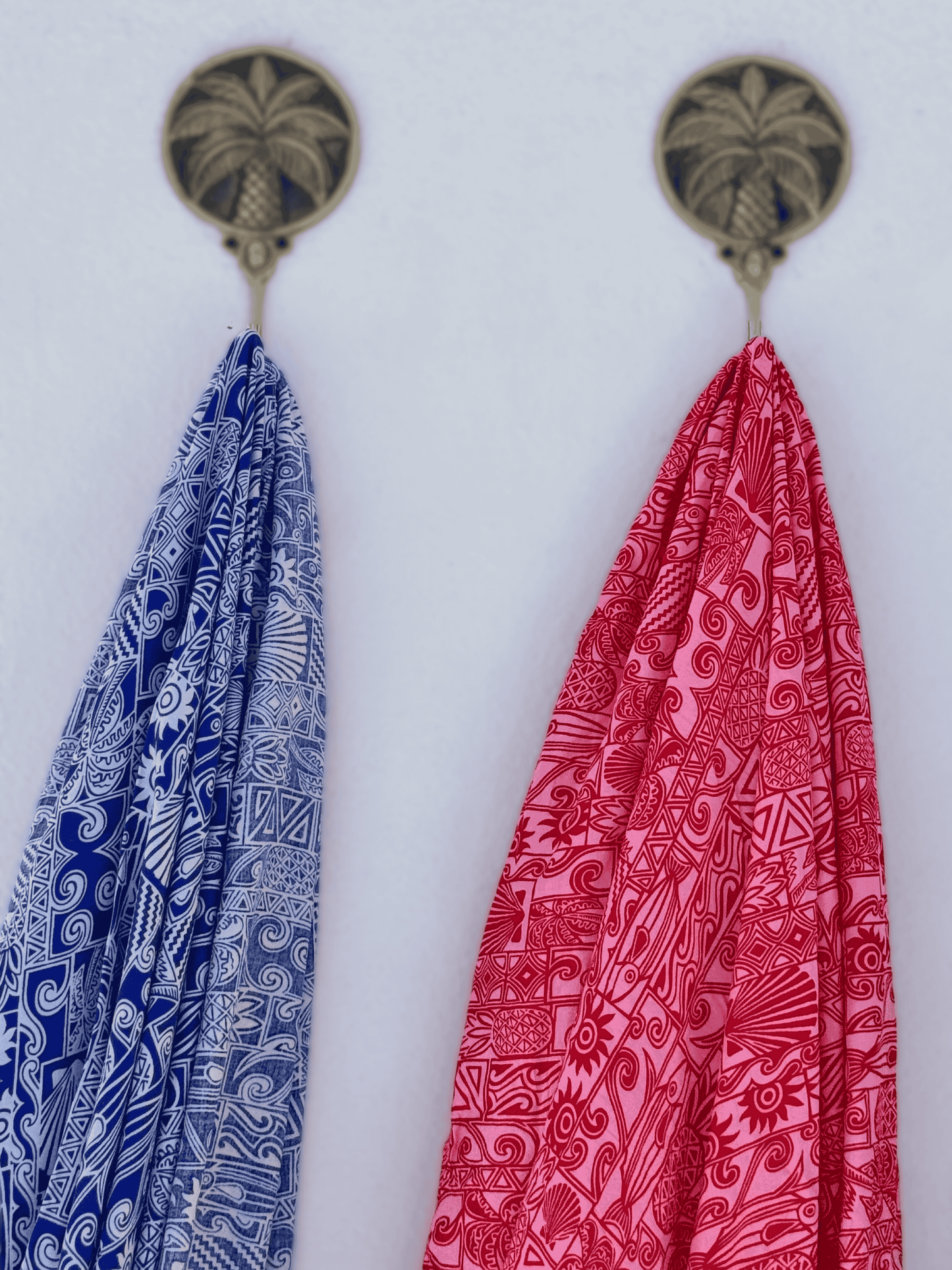 Two patterned sarongs hanging from decorative hooks on a white background