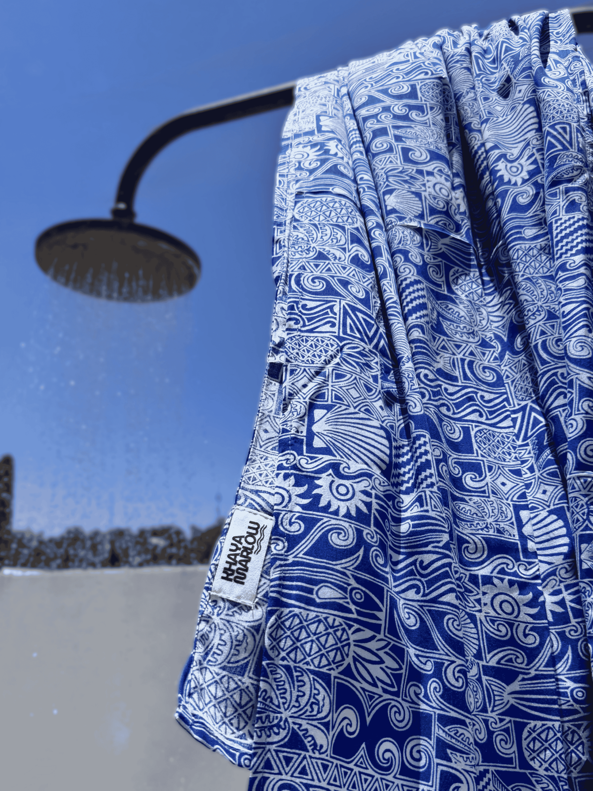 Blue and white patterned sarong hanging from a shower head outdoors.