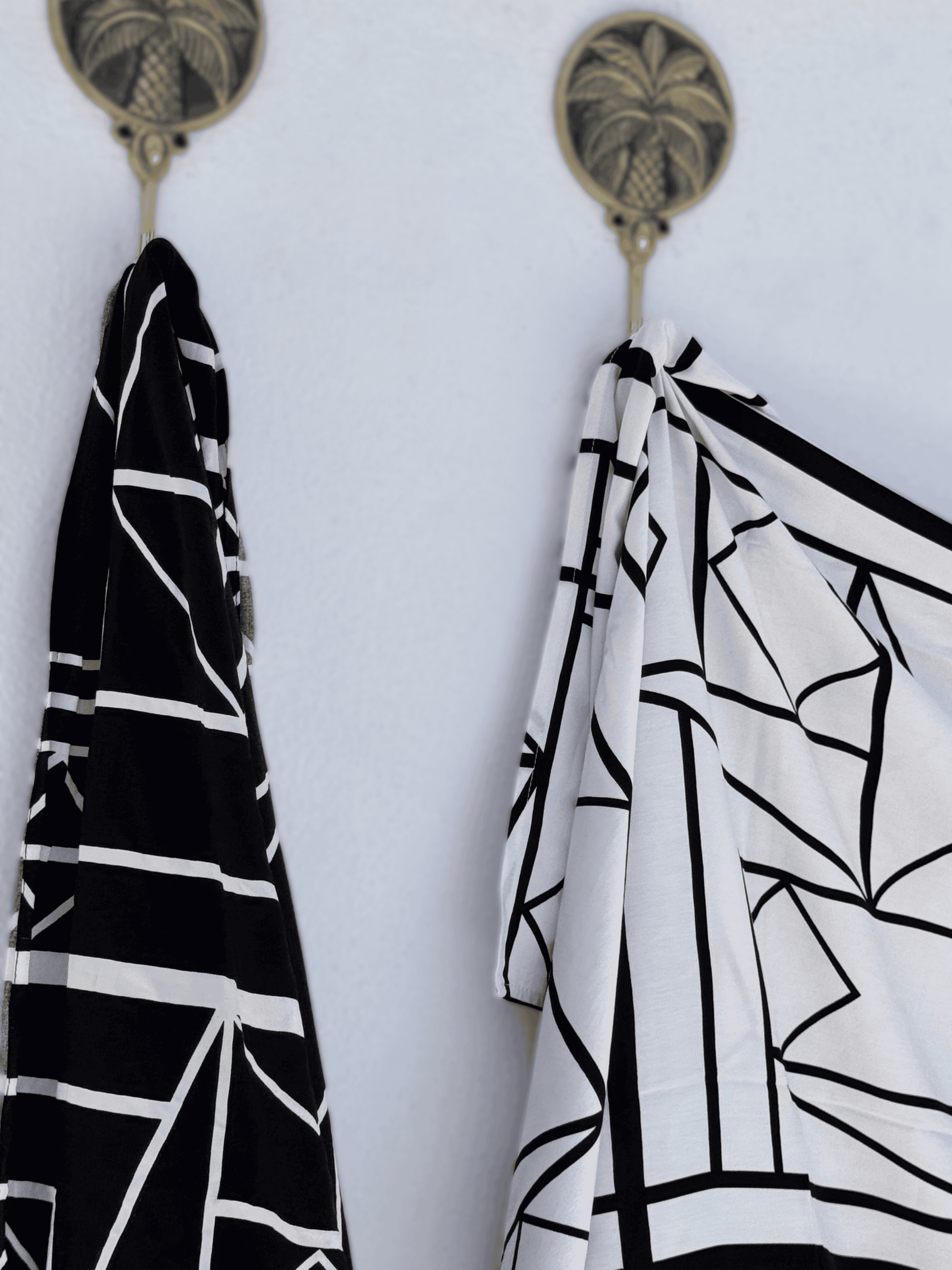 Two black and white patterned sarongs hanging on hooks against a white background.