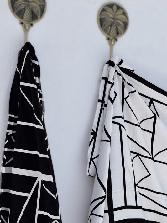 Two black and white patterned sarongs hanging on hooks against a white background.